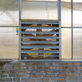 Louvered metal vent set into a brick wall beneath translucent greenhouse panels