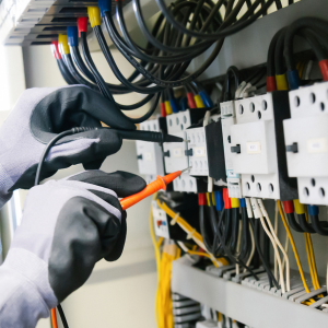 Technician using tools to inspect electrical wiring in a control panel