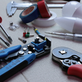 Assorted electrical tools and tape on a work surface, including wire strippers, pliers, screws, and connectors