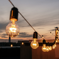 String lights glowing at dusk over a rooftop patio with a city skyline in the background