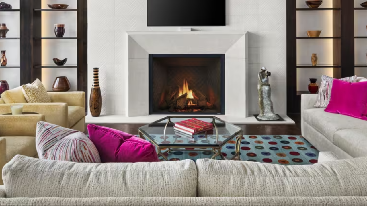 Modern living room with a lit fireplace, beige sectional, bright pink pillows, and glass coffee table
