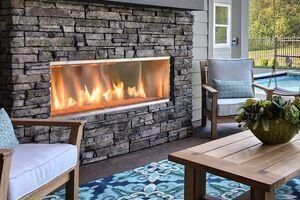 Outdoor patio with stone fireplace, cushioned chairs, and wooden coffee table on patterned rug