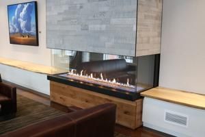 Modern fireplace with glass flame box beneath a large gray stone mantle in a contemporary room