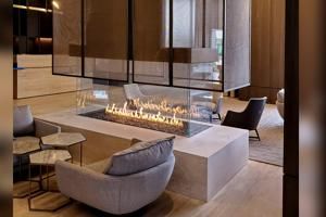 Modern lobby with a rectangular fire pit, gray chairs, and warm wood-and-glass decor