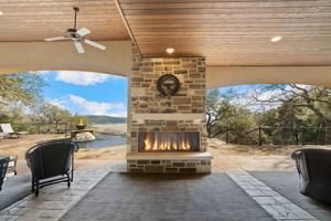 Covered patio with stone fireplace, seating, and a view of a lake and trees