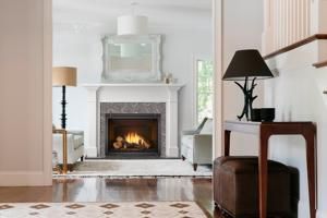 Elegant living room with a lit fireplace, white mantel, and dark side table with lamp