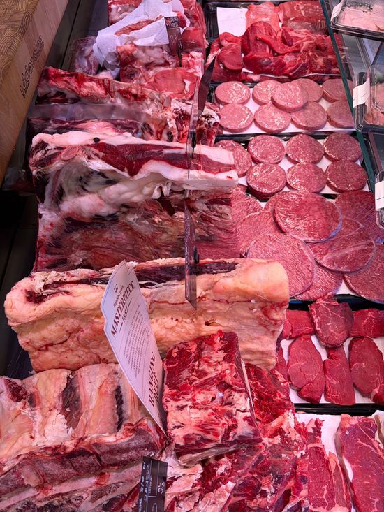 Banco di macelleria con esposizione di tagli assortiti e salsicce in vassoi rossi sotto una vetrina.