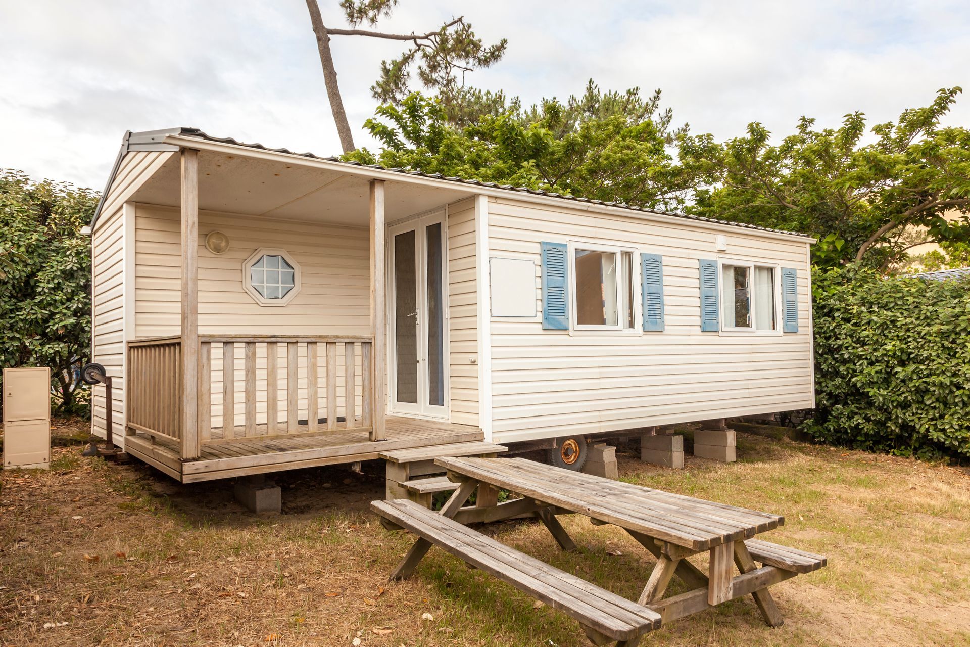 Mobile home with a small covered porch and picnic table in a landscaped outdoor setting. Mobile home with a small covered porch and picnic table in a landscaped outdoor setting.