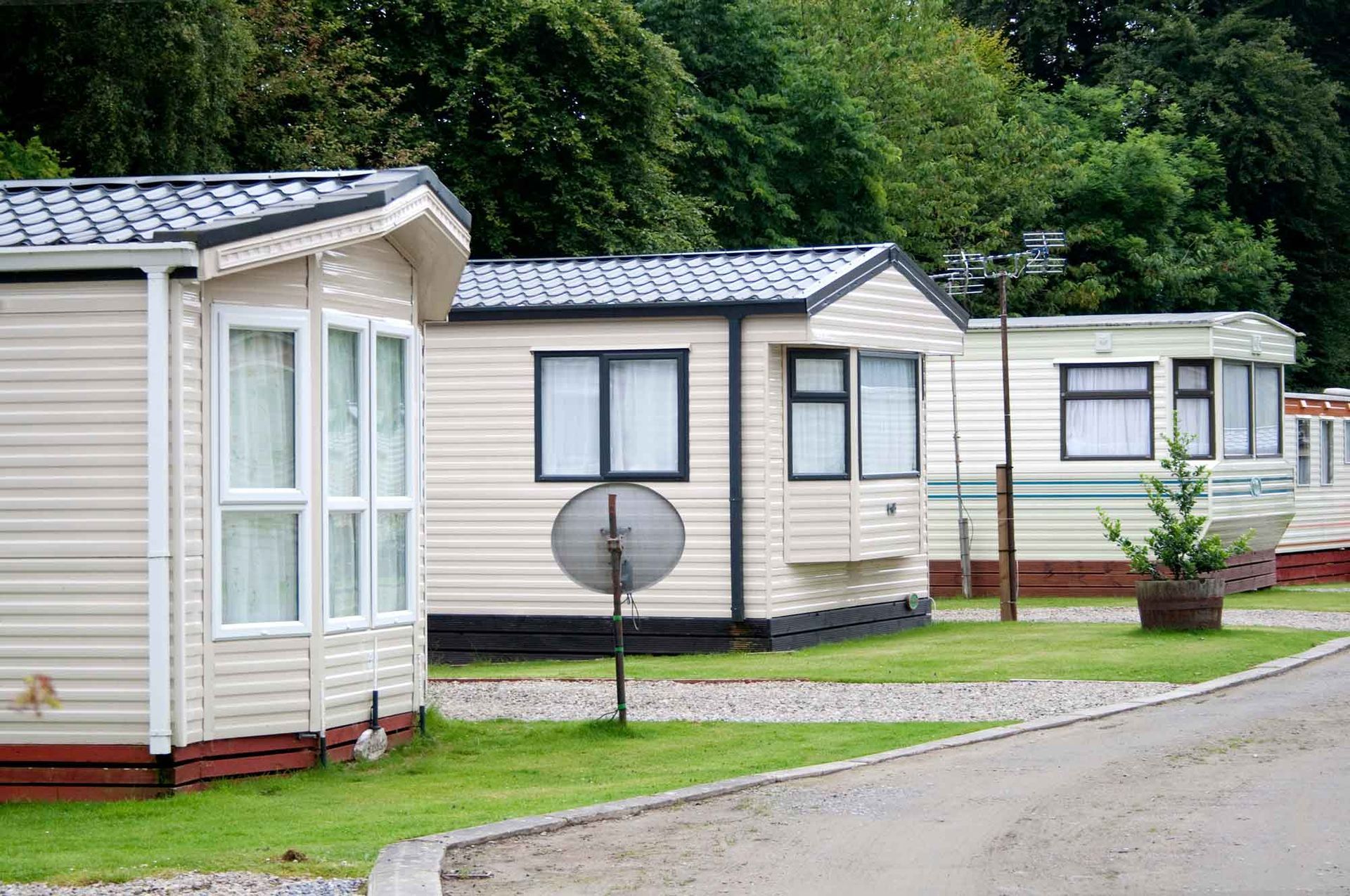 Row of mobile homes along a gravel path in a community surrounded by trees.