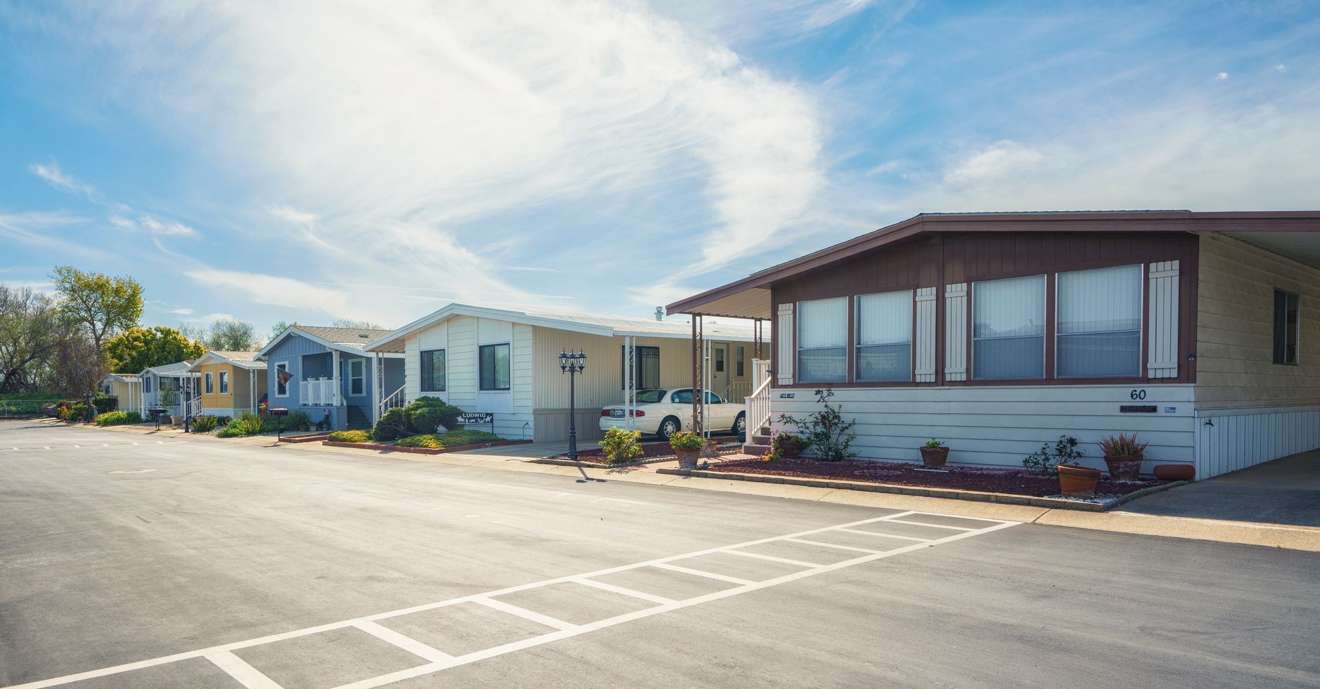 Row of mobile homes with large front windows and small landscaped yards on a sunny day.