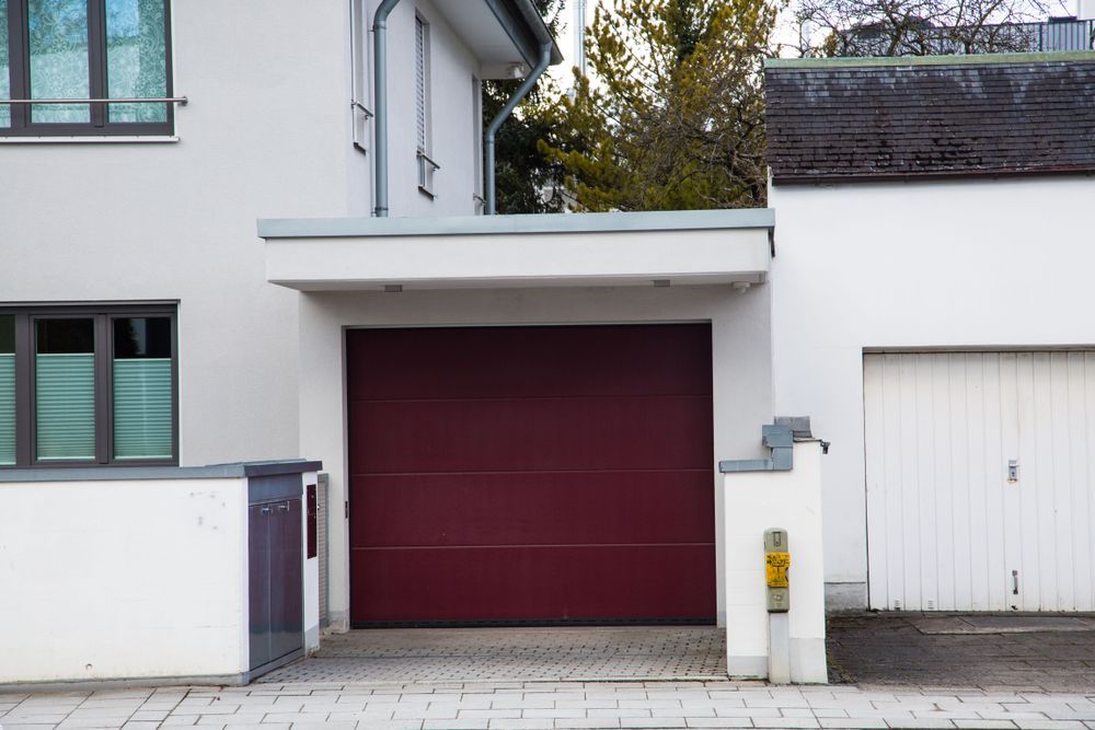 A Burgundy Garage Door in a White Building Facade — Axcess Garage Doors in Yeppoon, QLD