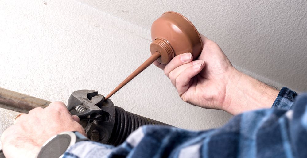 Person Lubricating a Garage Door Spring With a Brown Oil Can — Axcess Garage Doors in Yeppoon, QLD