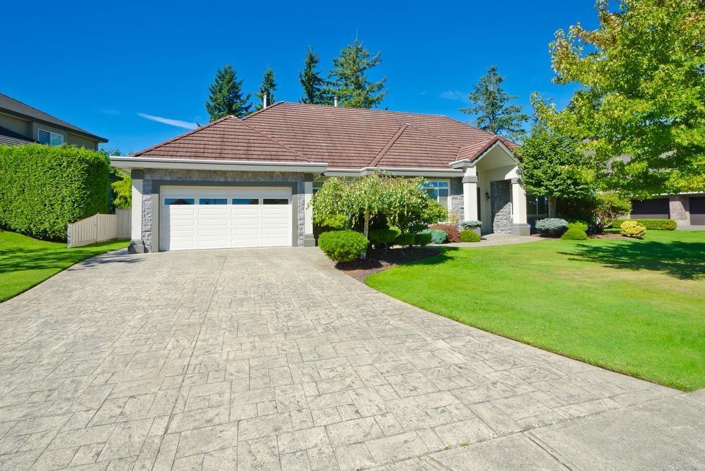 House With Concrete Driveway, Green Lawn, Blue Sky, and Garage Door — Axcess Garage Doors in Yeppoon, QLD