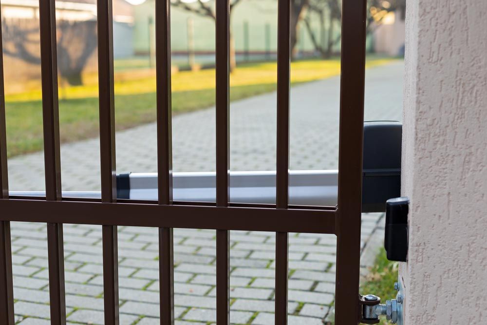 Brown Metal Gate With Automated Arm, Set Against a Paved Driveway and Beige Wall — Axcess Garage Doors in Yeppoon, QLD