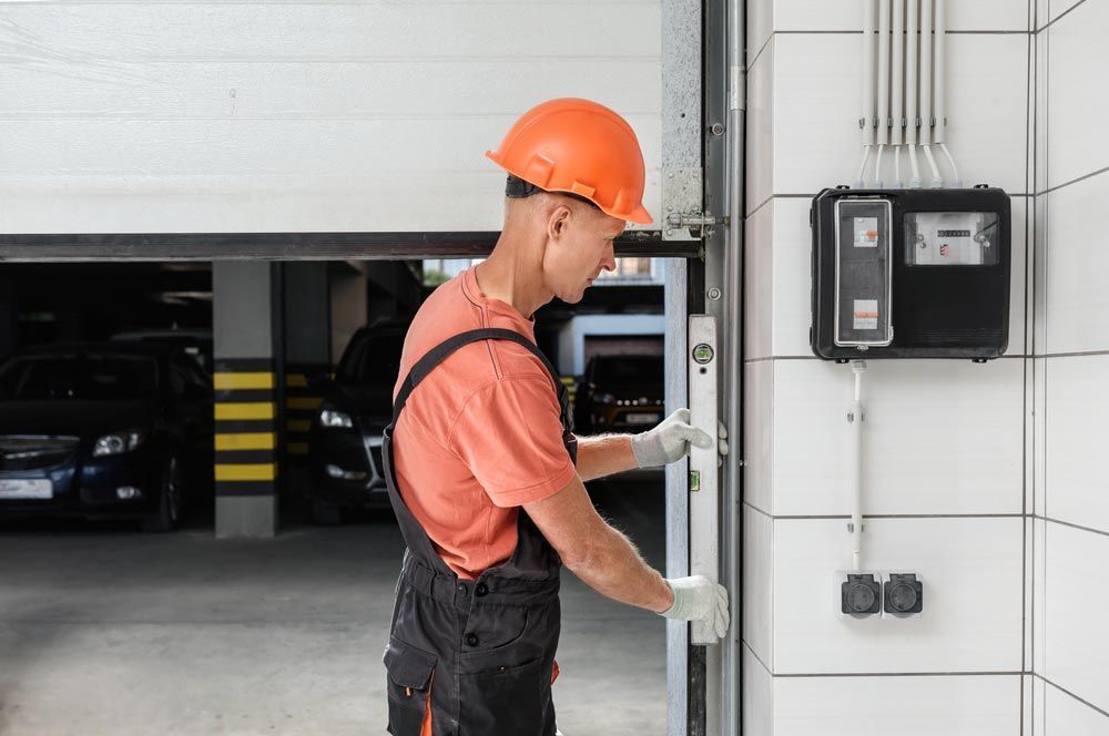 Man in Orange Hard Hat and Overalls Inspects Garage Door Mechanism — Axcess Garage Doors in Yeppoon, QLD
