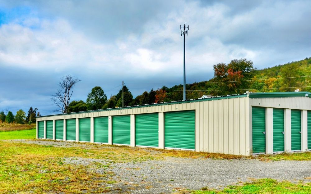 Storage Units With Green Doors Sit on a Gravel Lot — Axcess Garage Doors in Yeppoon, QLD