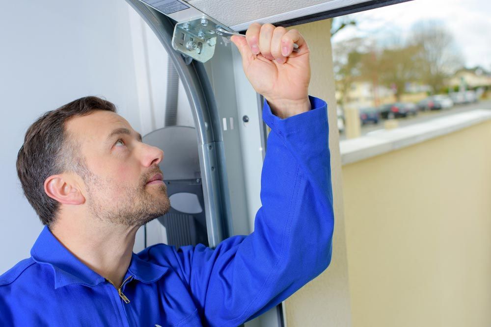 Man in Blue Jumpsuit Inspecting Garage Door Hardware — Axcess Garage Doors in Yeppoon, QLD