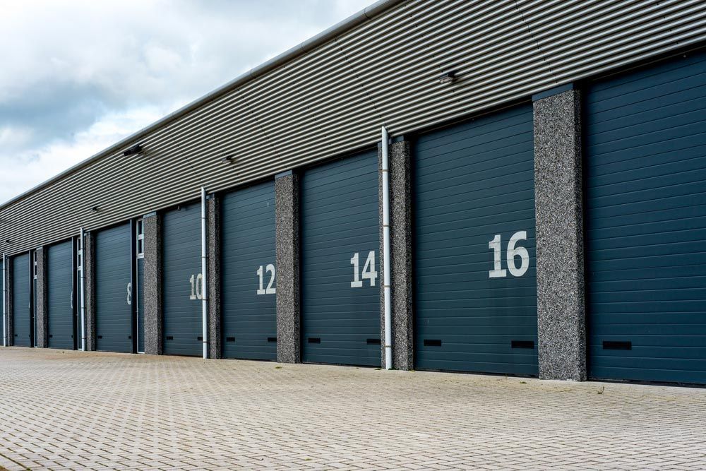 Self-storage Units, Dark Blue Doors With White Numbers, Brick Exterior, Overcast Sky — Axcess Garage Doors in Yeppoon, QLD