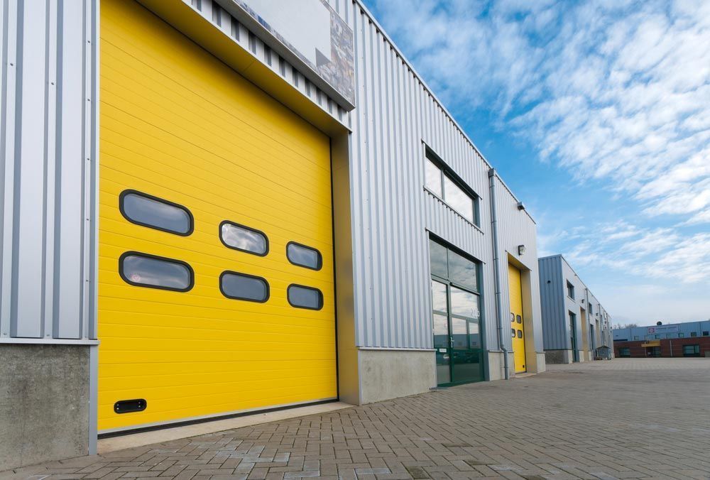Yellow Industrial Garage Door With Windows, on a Warehouse Building — Axcess Garage Doors in Yeppoon, QLD
