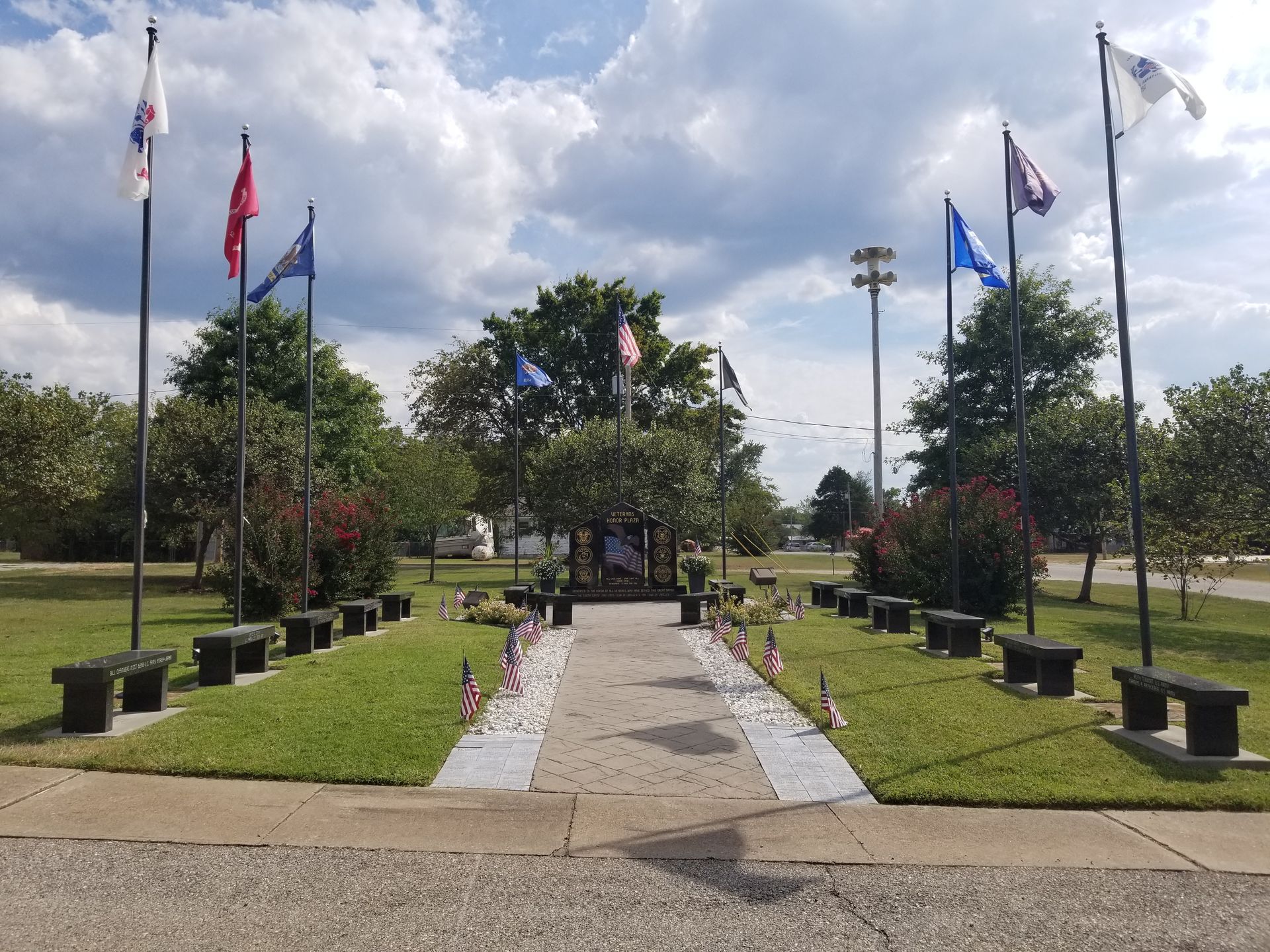 A park with a row of benches and flags flying in the wind.