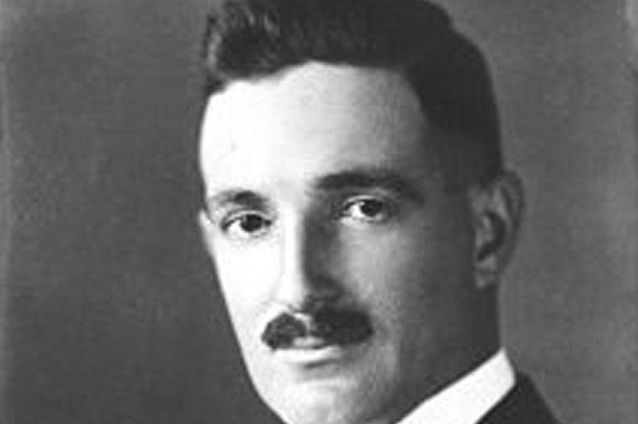 A black and white photo of a man with a mustache wearing a suit and tie.