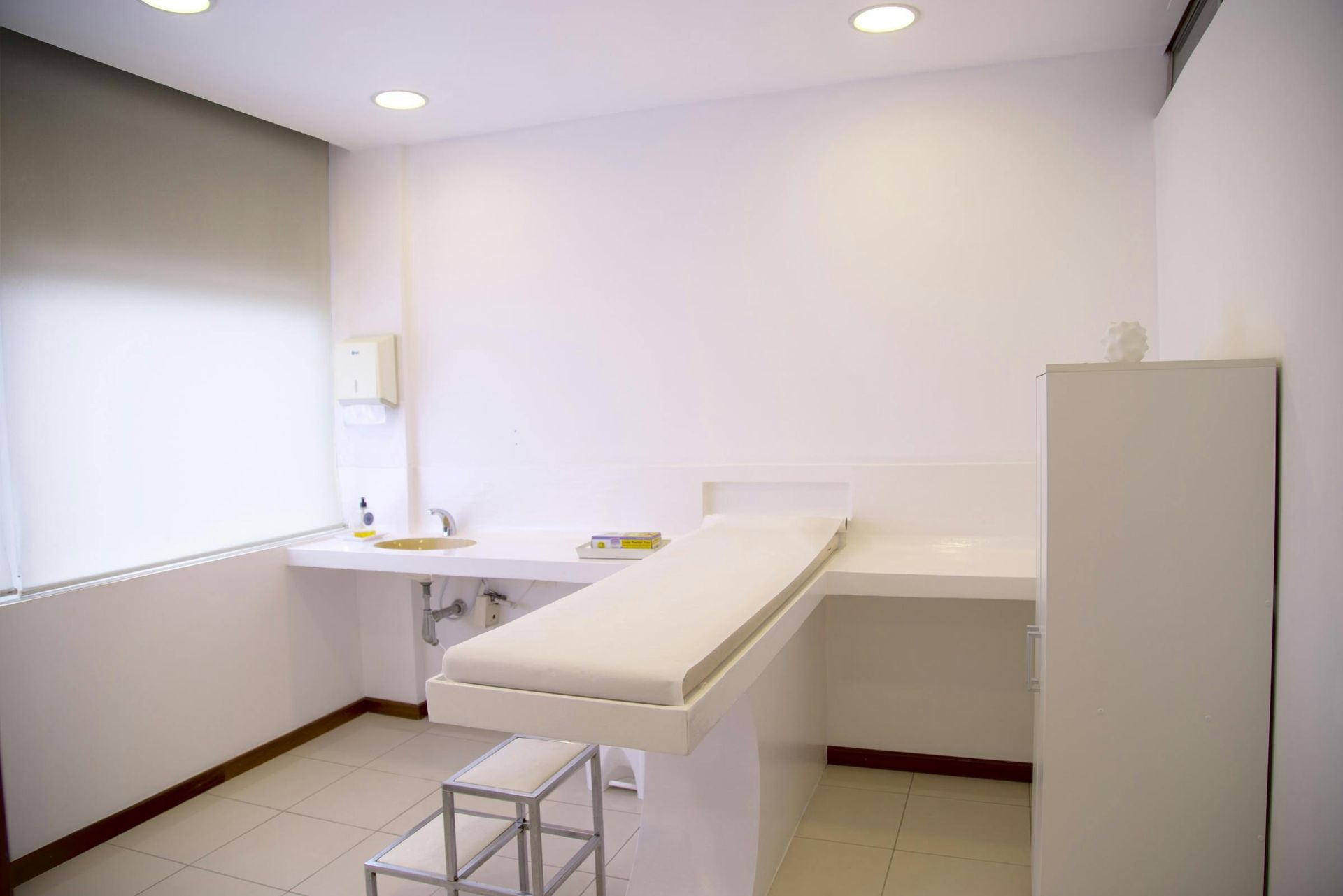 Examination room with white walls, examination table, desk, and stool.