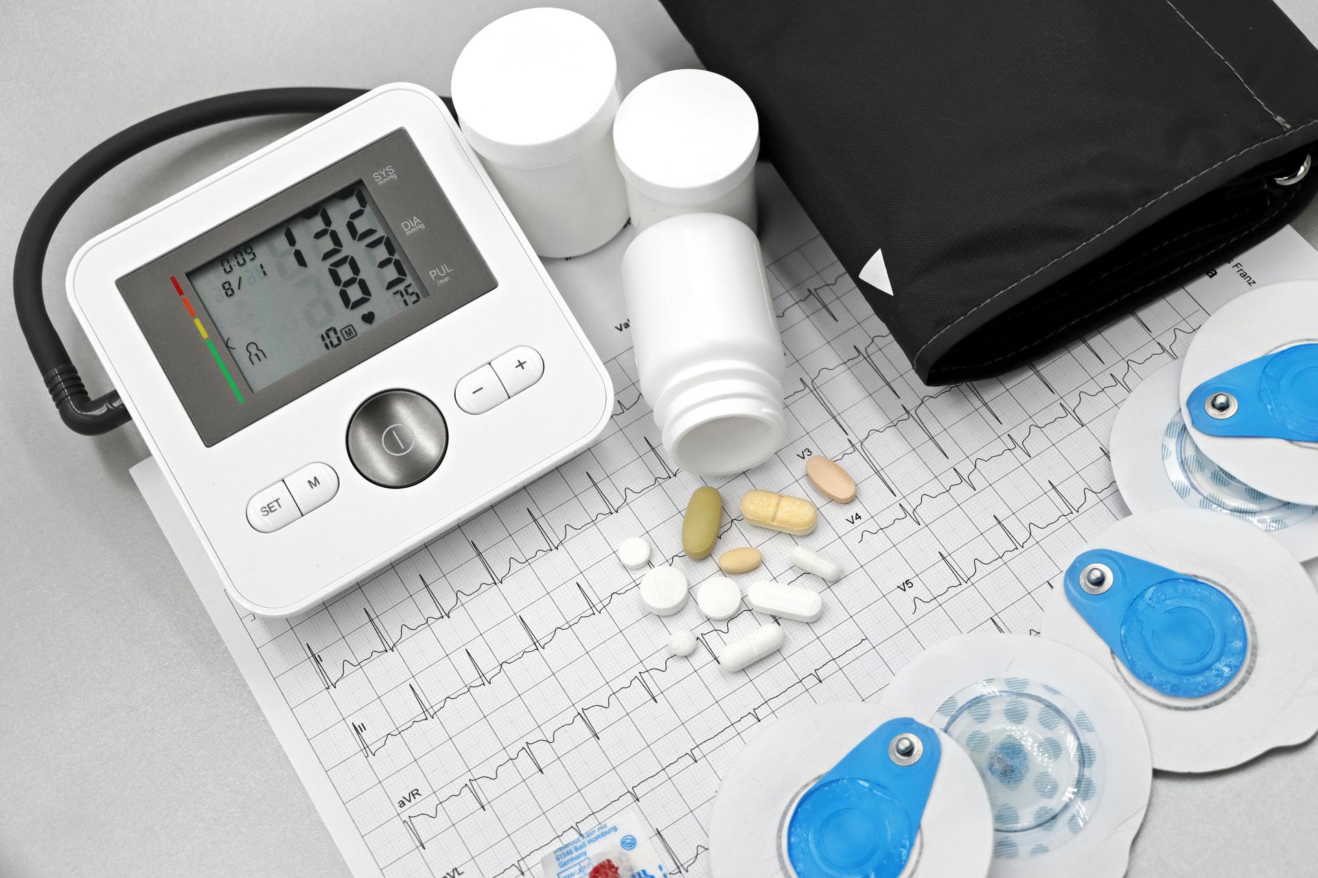 Blood pressure monitor, pill bottles, pills, EKG pads on electrocardiogram printout.
