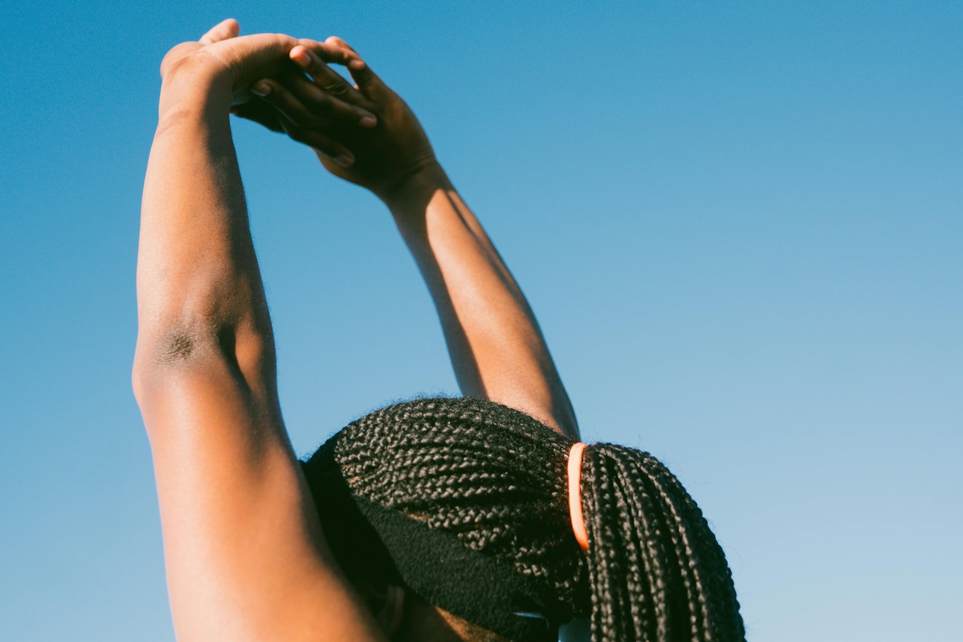 Person stretching arms overhead against a clear blue sky.