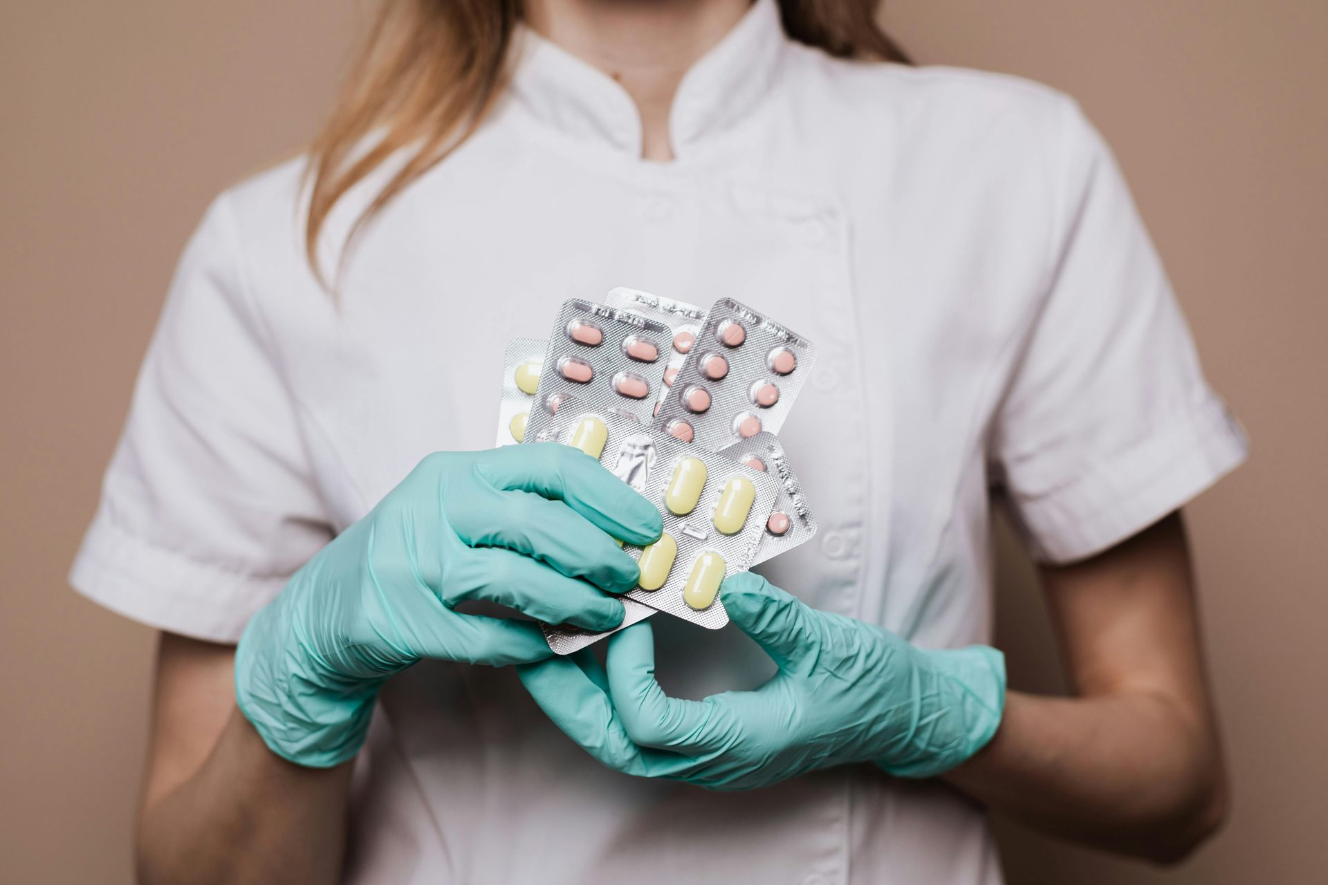 Person in white uniform and blue gloves holds multiple pill blister packs.