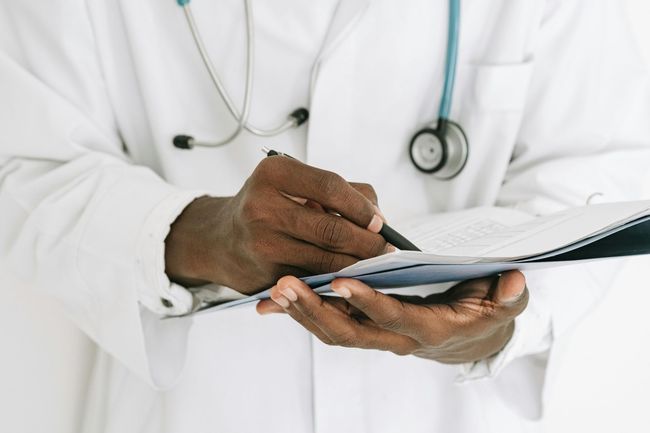 Doctor writing on a clipboard, stethoscope around their neck.