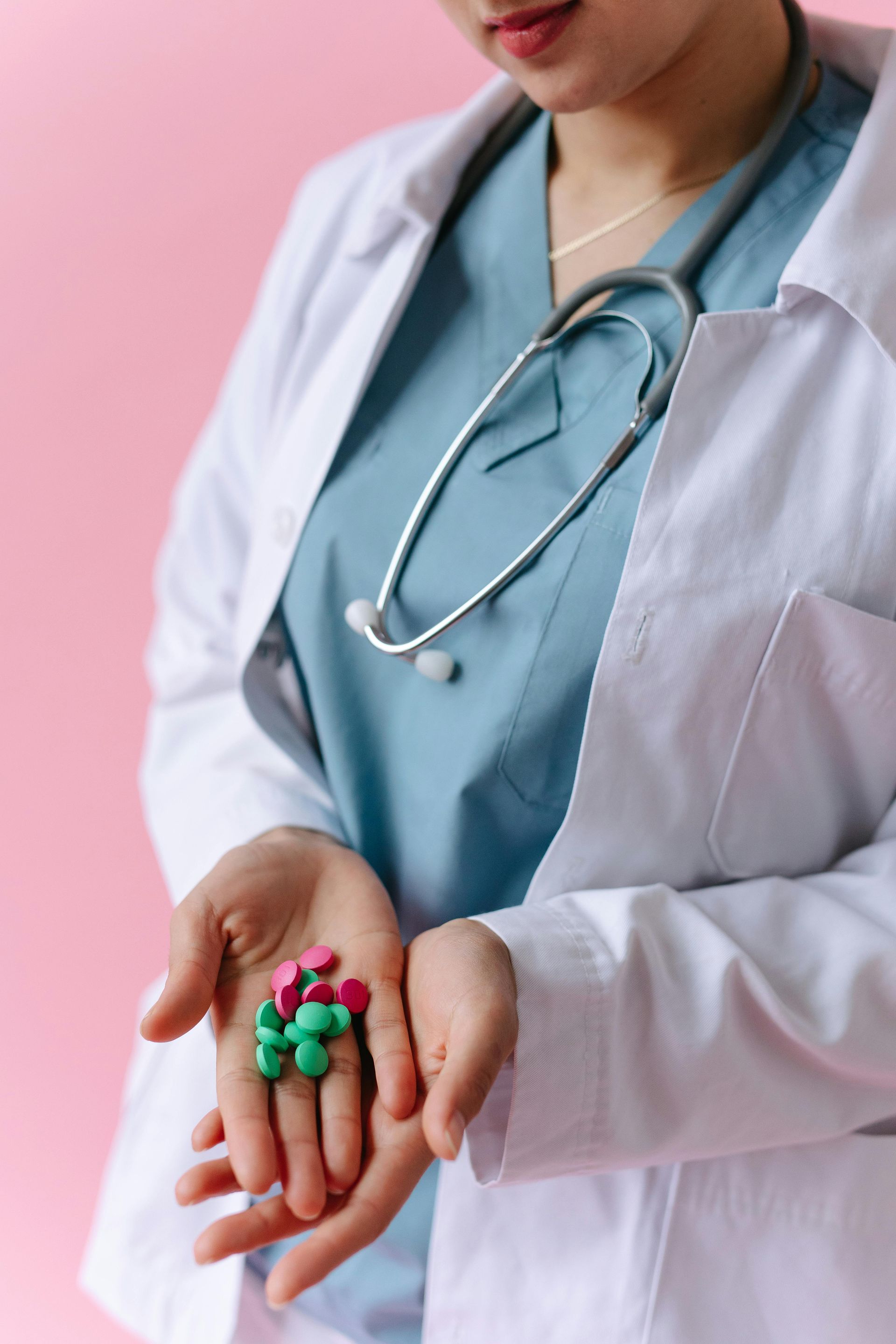 Doctor holding a handful of colorful pills, wearing a white coat and stethoscope.