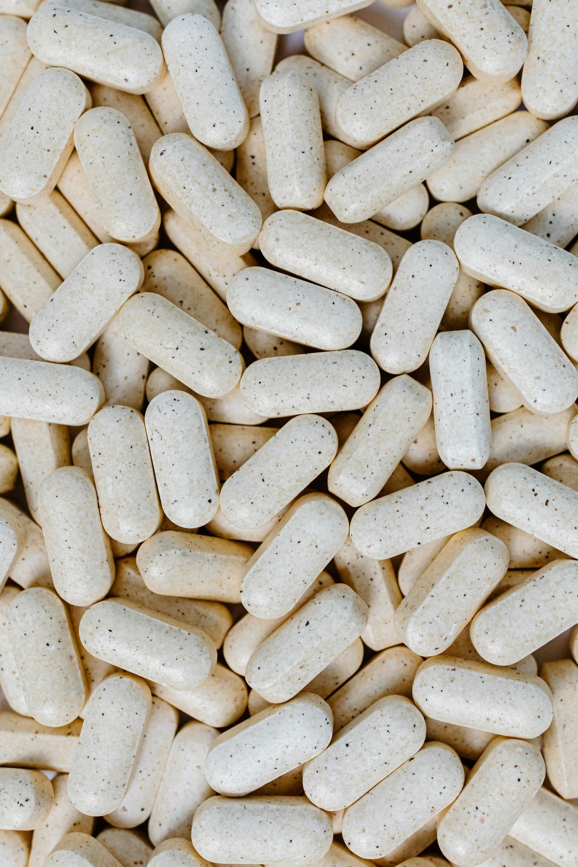 Pile of light beige oval capsules, speckled with dark flecks.