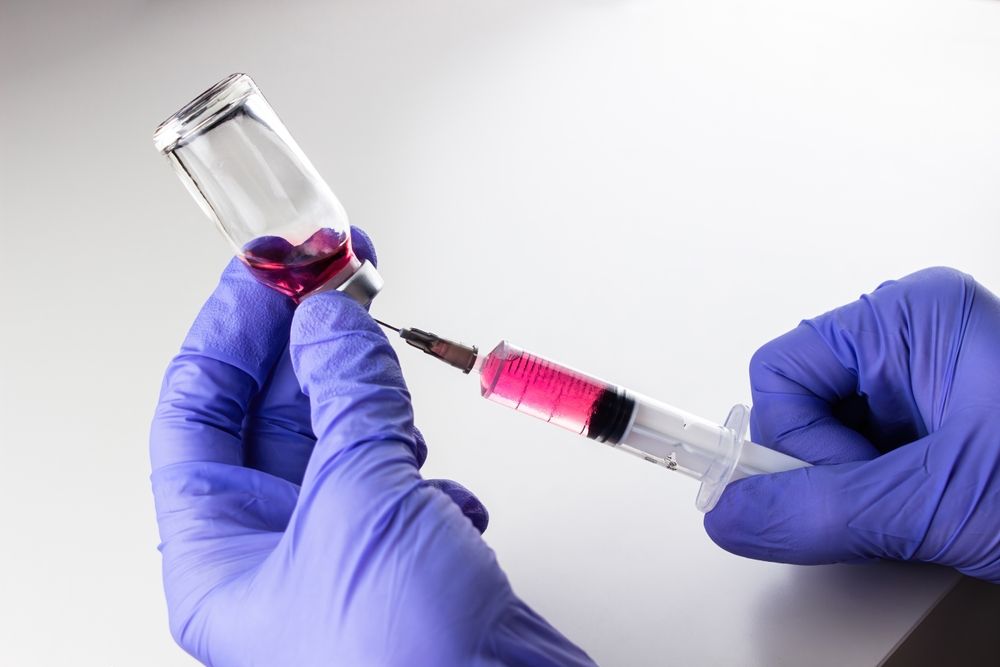 Hands in blue gloves filling a syringe with pink liquid from a vial.