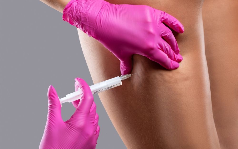 Hands in pink gloves injecting leg with a syringe. Grey background.
