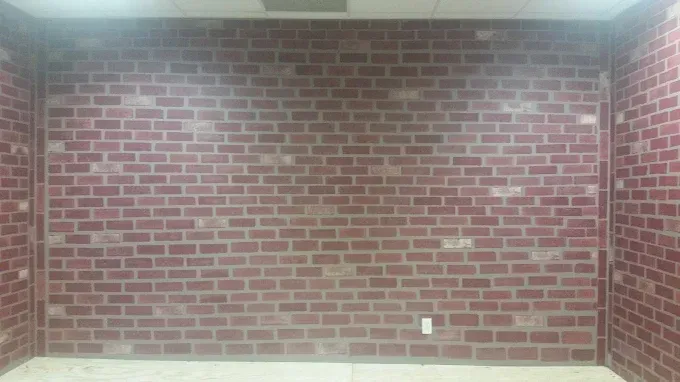 Red brick wall in an empty room with a light fixture on the ceiling and an electrical outlet.