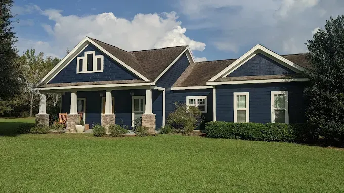 Blue house with porch, white trim, and a green lawn under a blue sky.
