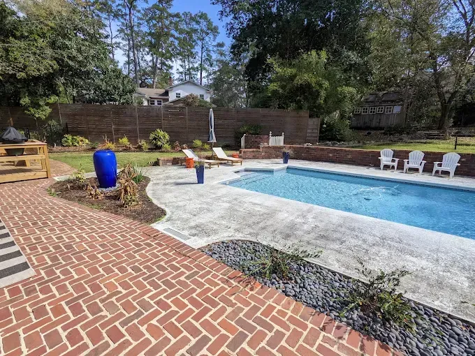 Brick patio leads to a backyard pool with lounge chairs and a blue vase on a sunny day.