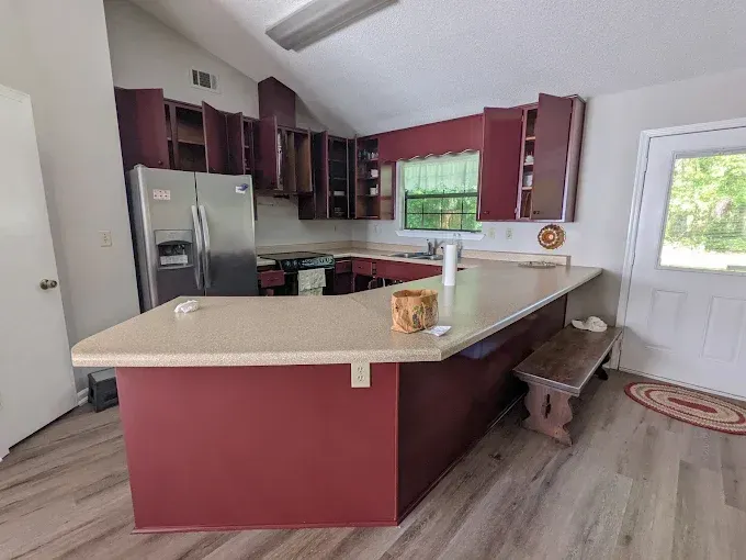 Kitchen with maroon cabinets, a beige countertop, stainless steel refrigerator, and light wood floors.