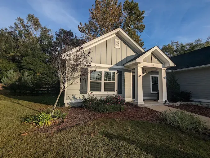 Small, light blue house with white trim, porch, and dark gray shutters on a sunny day.