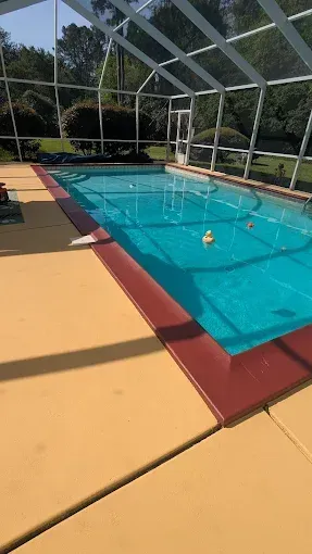 A rectangular pool with teal water, surrounded by tan decking and a screened enclosure.