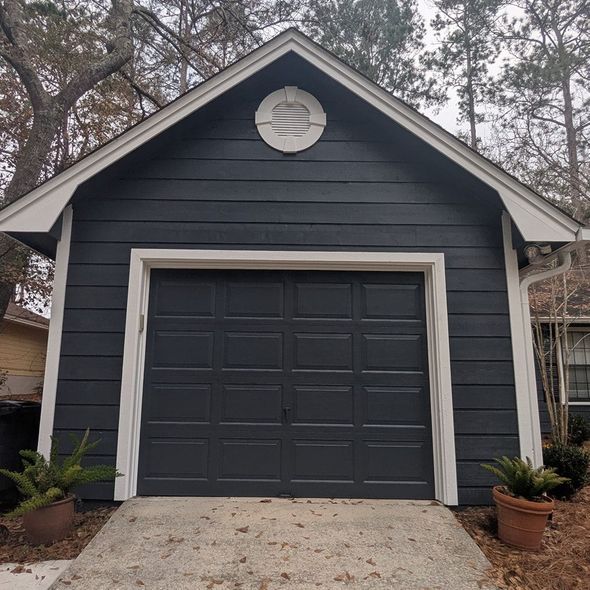 Dark gray garage with white trim, a circular detail, and two potted plants.