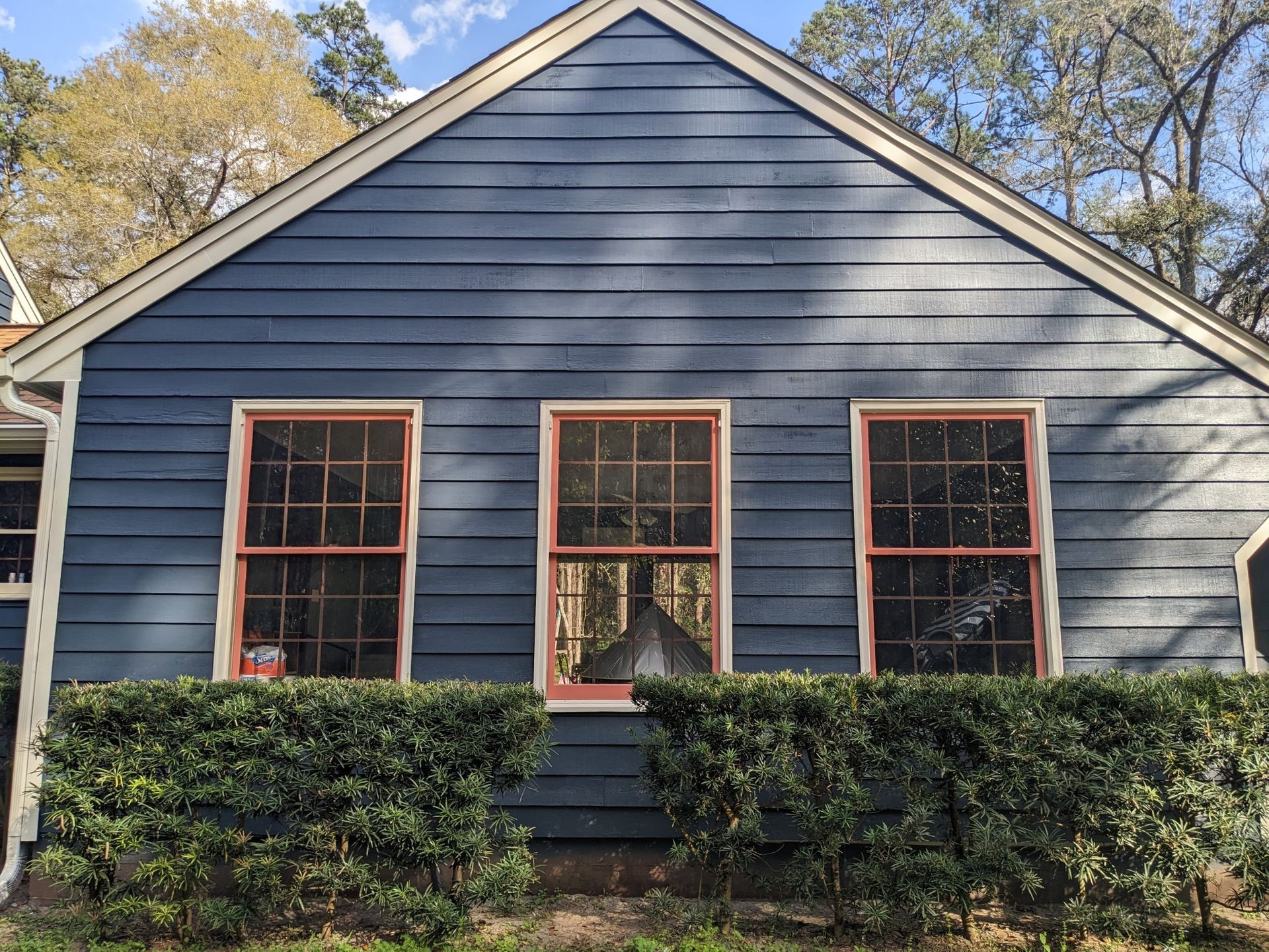 Blue house with pink window frames and three windows above a green hedge.