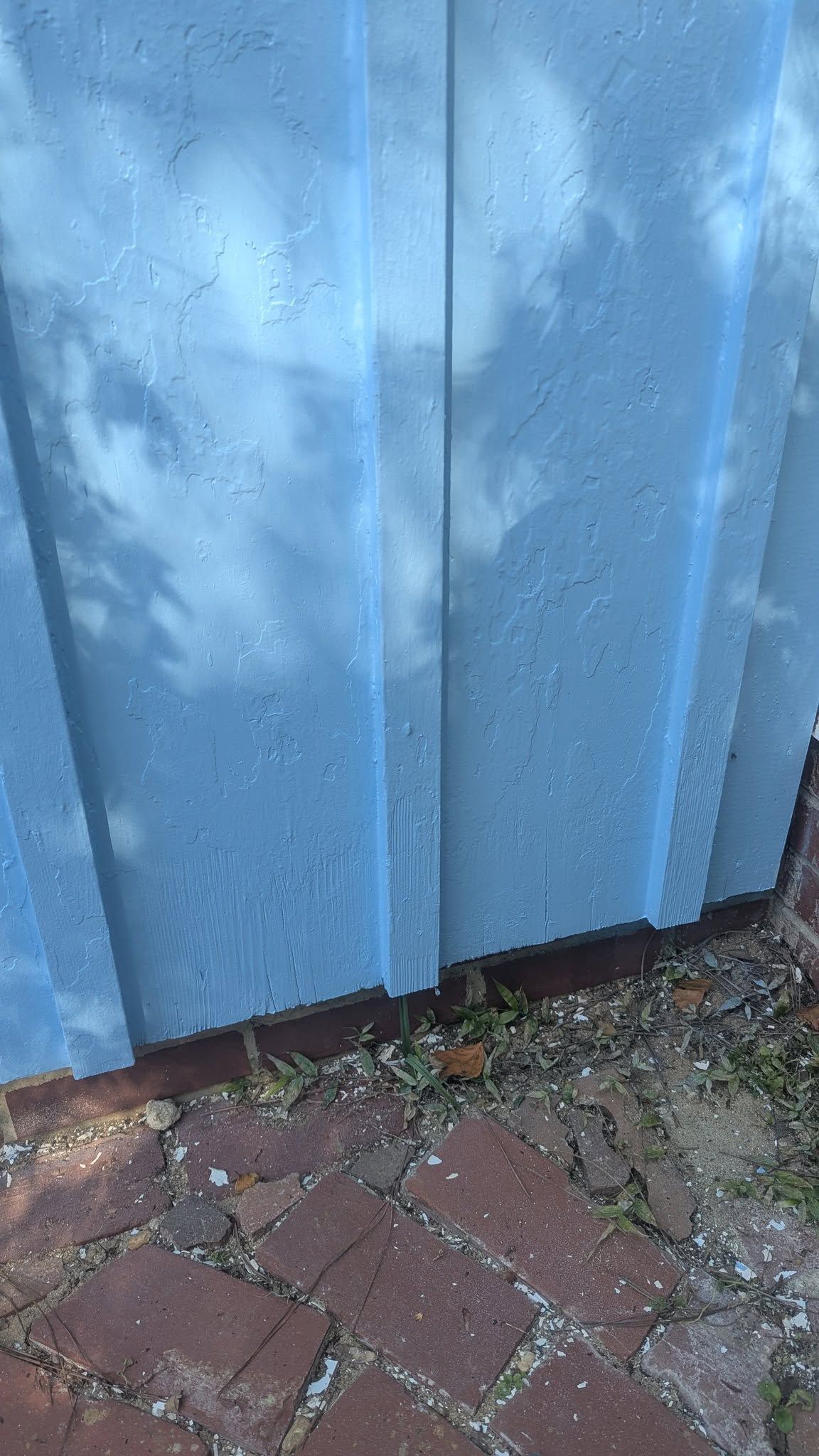 Blue corrugated metal siding with shadows, next to red brick paving.