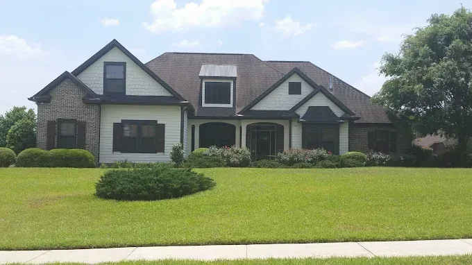 Two-story house with beige siding, brick accents, and a green lawn under a blue sky.