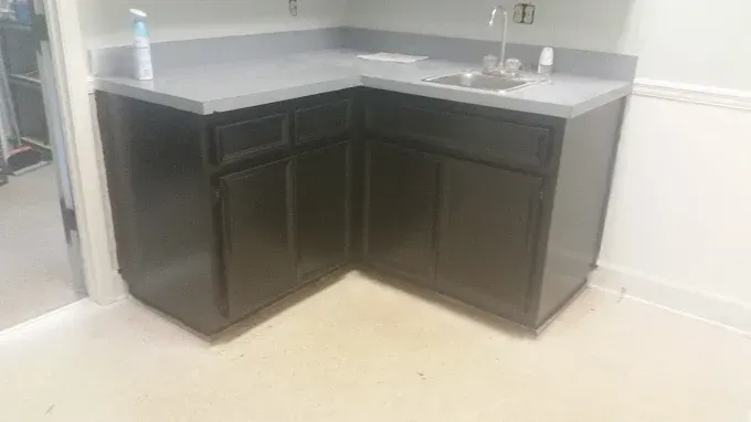 Dark cabinets with gray countertop, sink, and faucet in a corner.