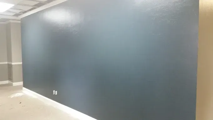 Dark blue painted wall in an empty room with white trim, and a partial view of the ceiling.