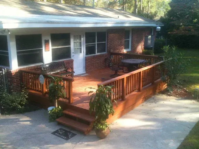Brick house with wooden deck, railing, steps, and potted plants; outdoor seating.