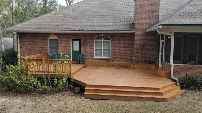Wooden deck attached to a brick house, with steps leading down to the yard.