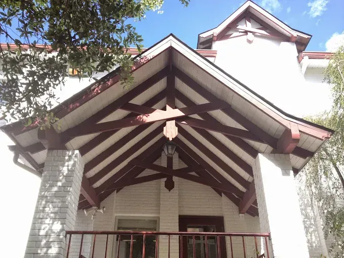 White house with red-brown wood beams and trim, under a blue sky.