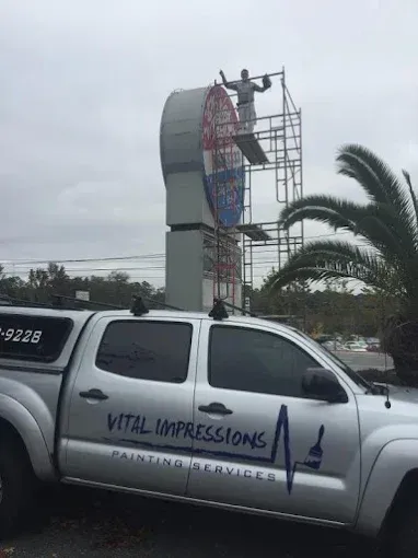 Man on scaffolding painting a large sign, truck of 